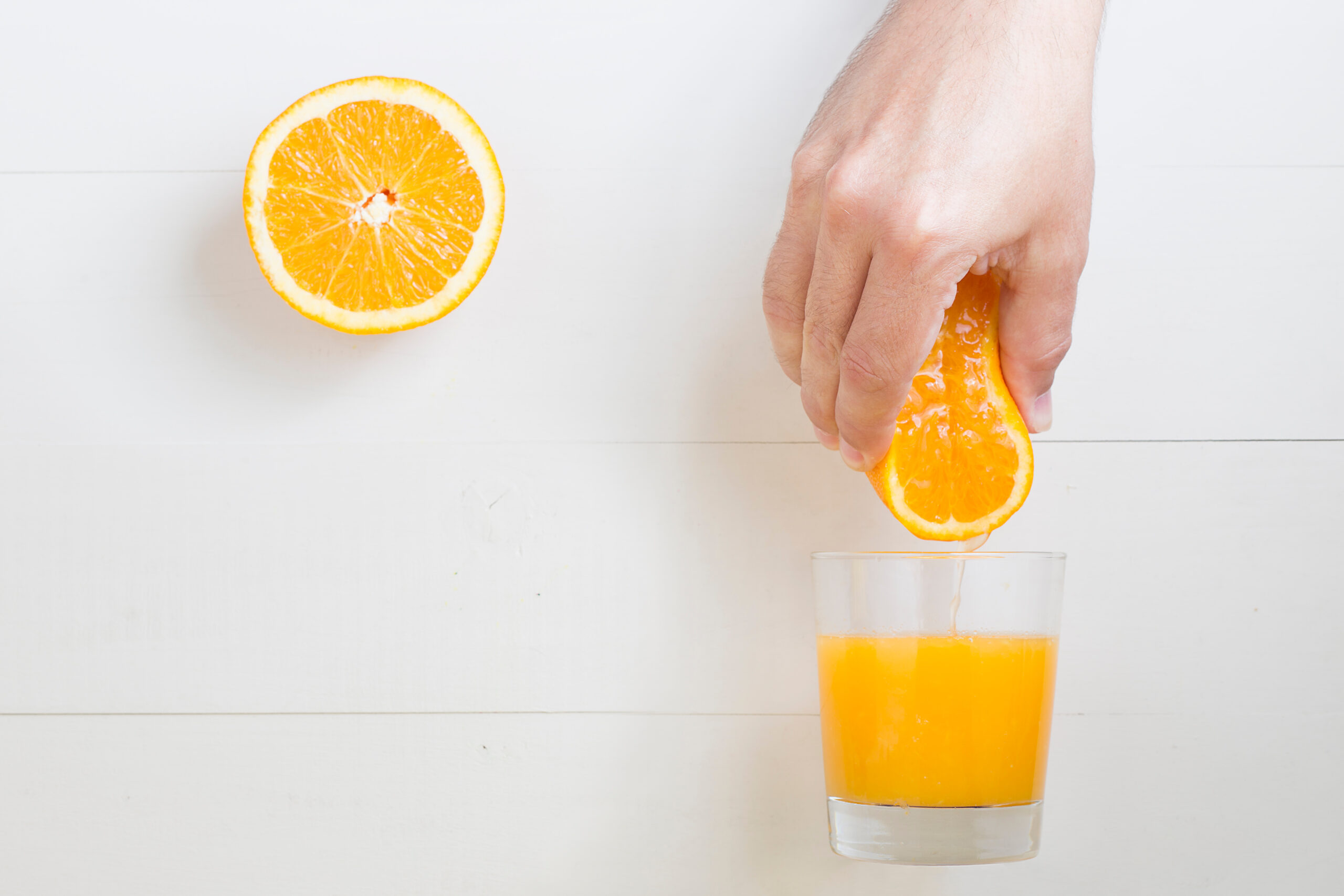 Man hand squeezing orange on orange juice glass